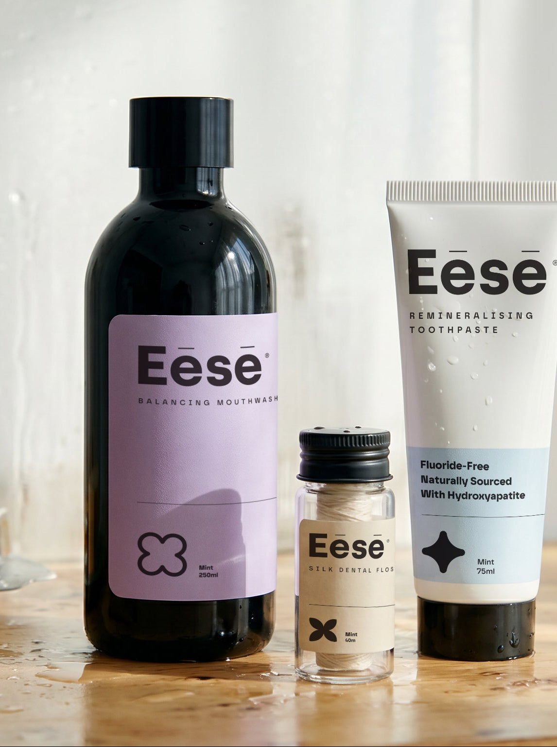 Three Eese oral care products arranged on a bathroom counter: best alcohol free and peroxide mouthwash, sls free toothpaste with hydroxyapatite, and silk and bee-waxed floss.