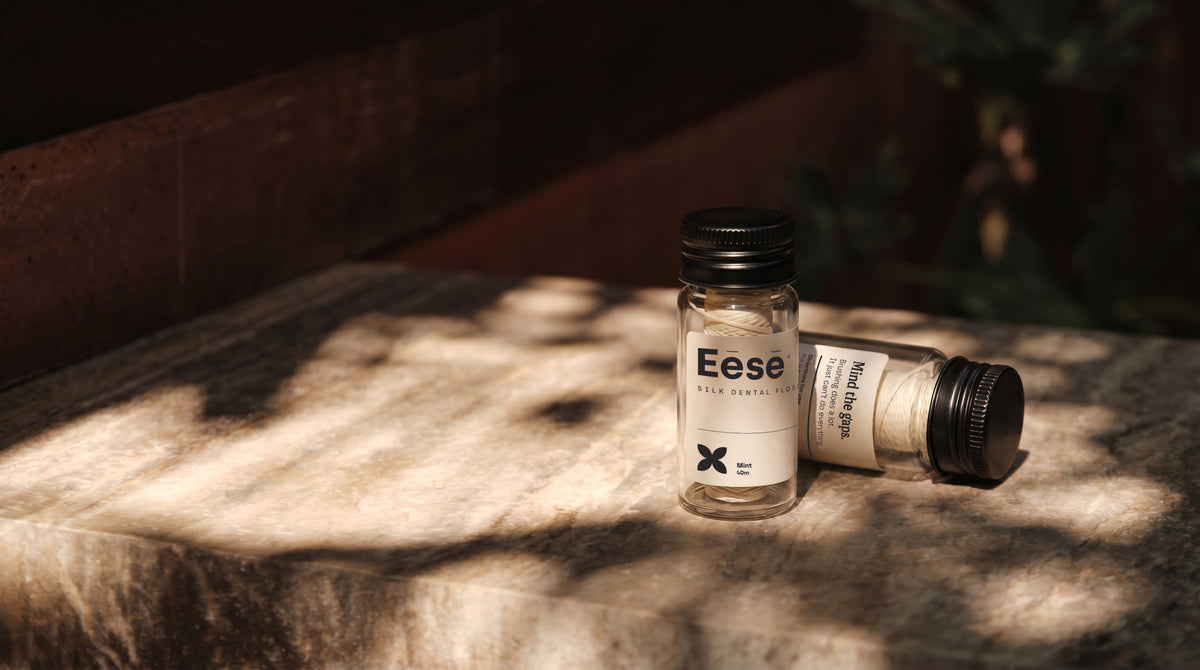 Eēsē silk dental floss in glass vials with black caps on a stone surface, bathed in warm natural light, a natural best floss for daily teeth flossing.